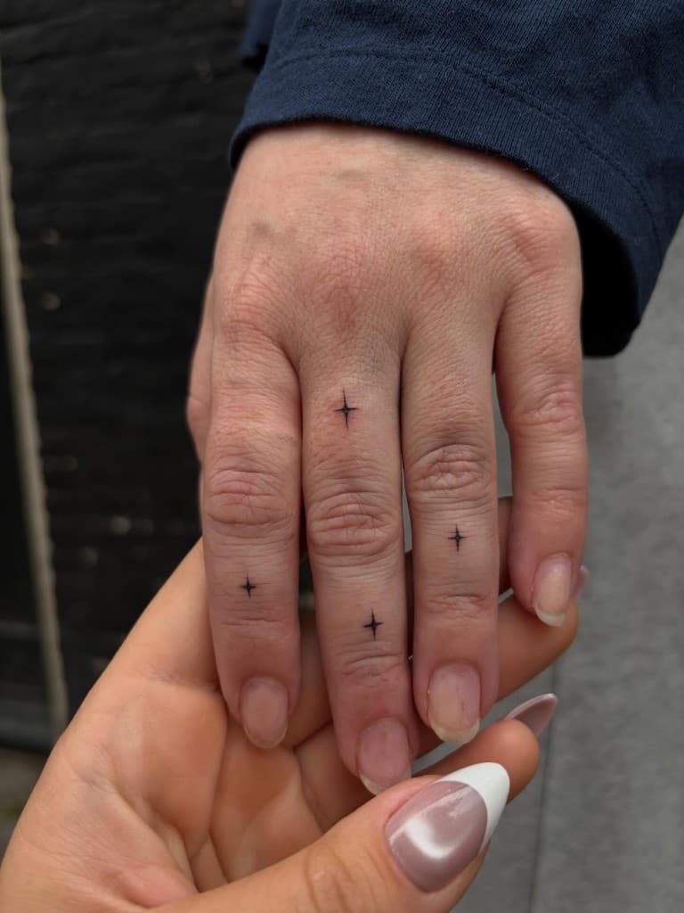 Four small fine-line star tattoos on the index, middle, and ring fingers.