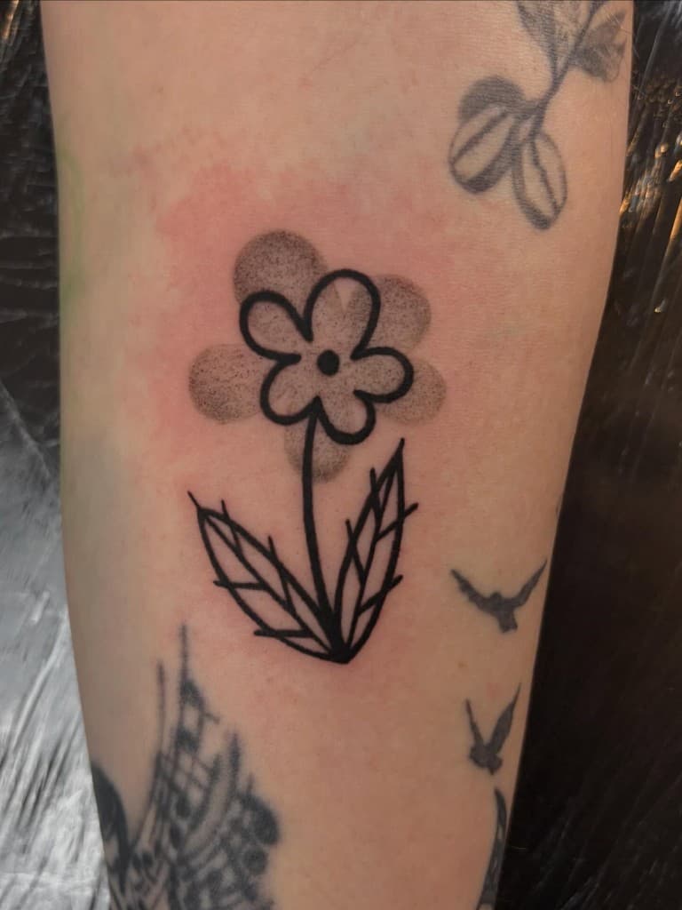Bold black flower tattoo with two leaves and a stippled shadow, photographed while fresh.